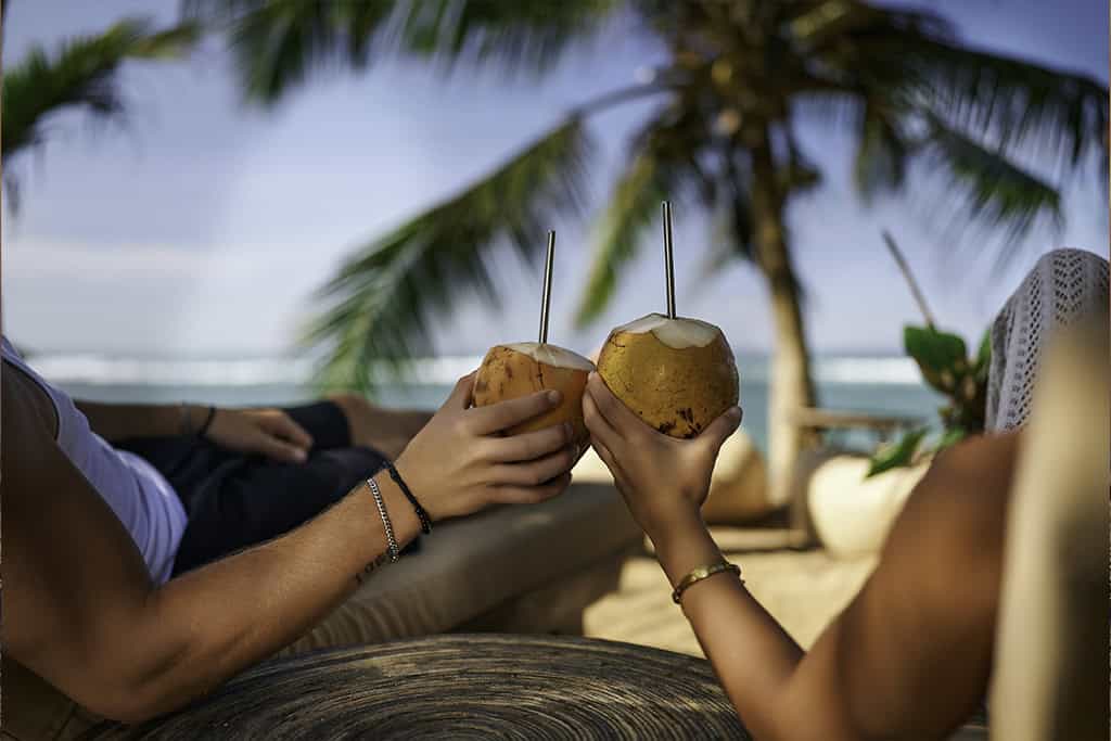 Couple relaxing on a tropical Sri Lankan beach, toasting with king coconuts